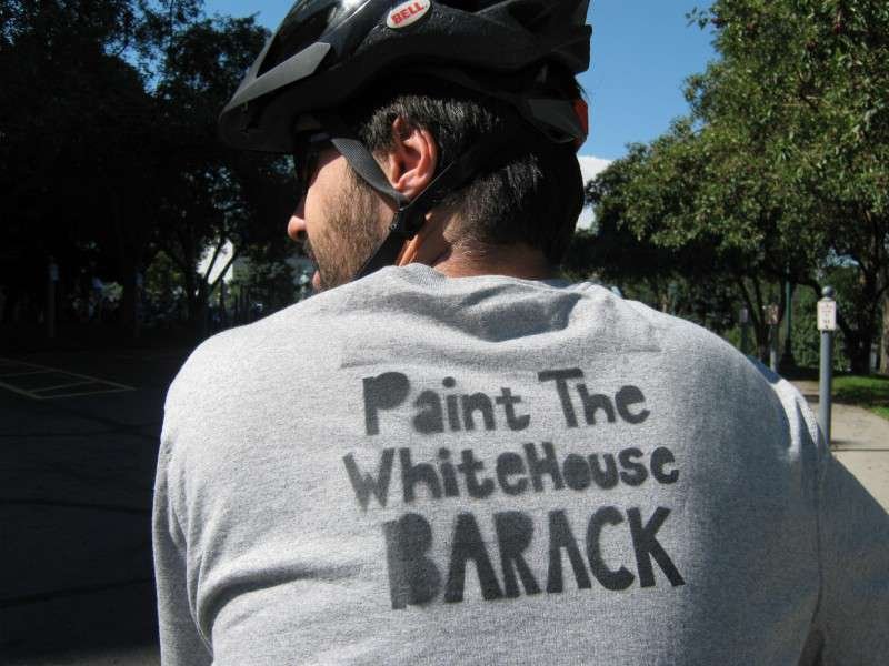 Back view of a cyclist wearing a shirt reading “Paint The WhiteHouse BARACK”