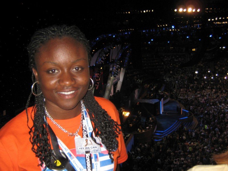 Sajdah smiling on the convention floor at night, arena and crowd visible behind her