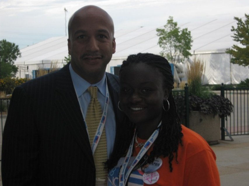 Sajdah smiling next to a man in a pinstripe suit outdoors at the 2008 DNC