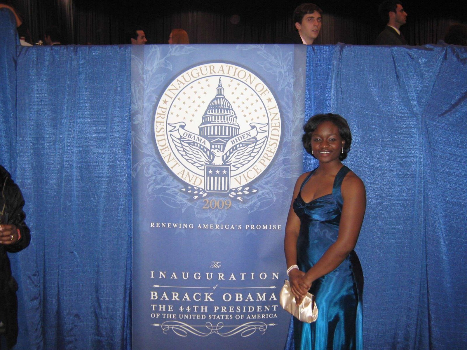 Sajdah in a blue evening gown standing beside an official 2009 inauguration banner