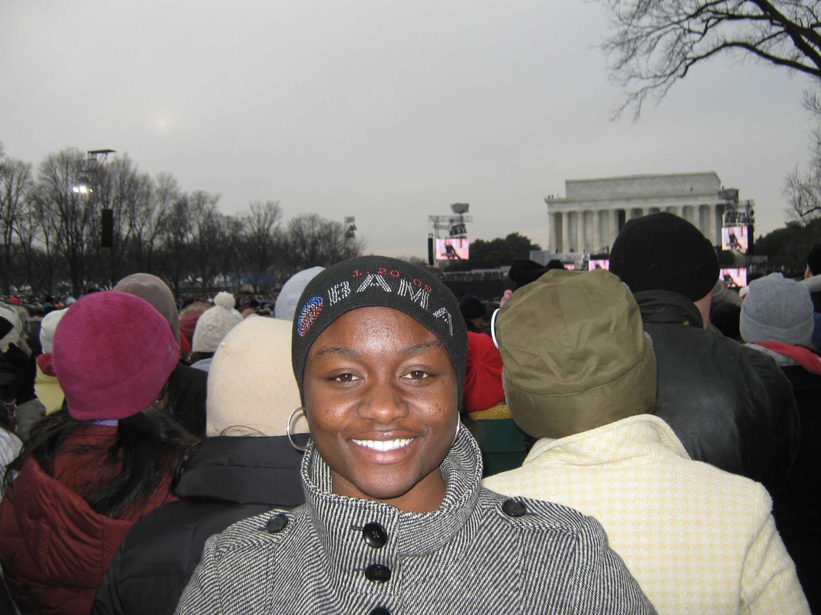 Sajdah smiling in a winter coat and beanie, a large crowd and the Lincoln Memorial behind her