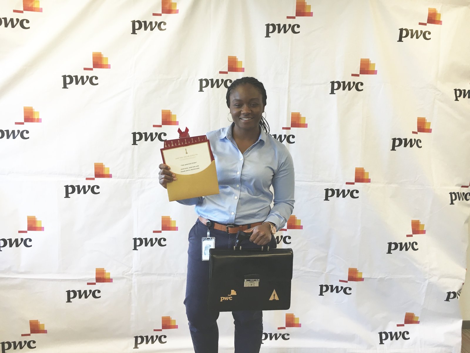 Sajdah holding a mock "Oscar goes to" envelope at a PwC event, standing with a PwC-branded briefcase