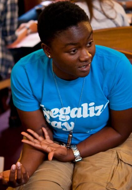 Sajdah wearing a "Legalize Gay" T-shirt, mid-conversation with her hands raised